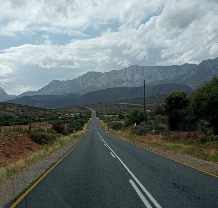 A clear highway road with magnificent views of the Swartberg mountain in the background on a cloudy day.